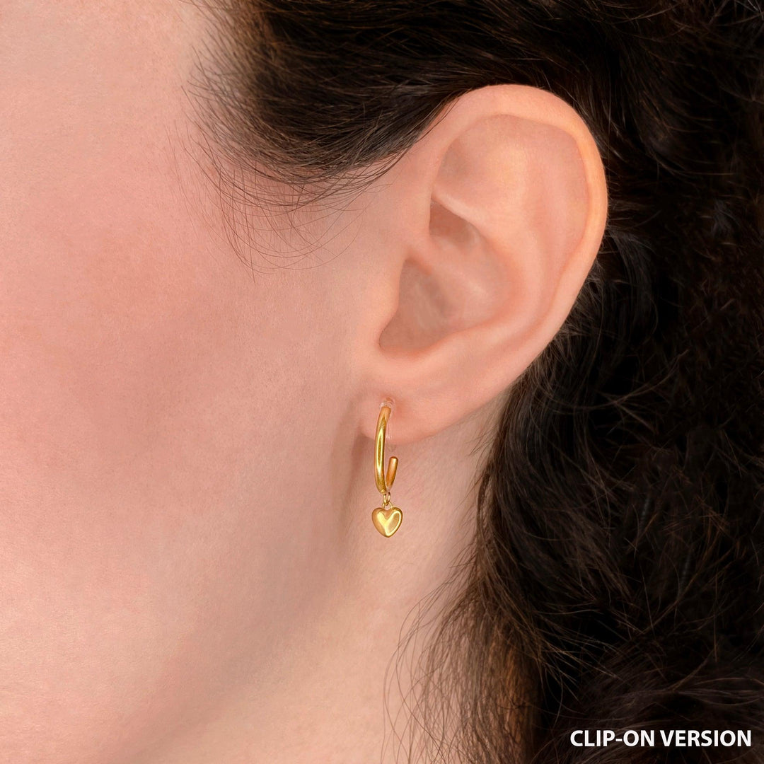 Thin huggie hoop clip on earrings with dangling heart charm in gold worn on the ear